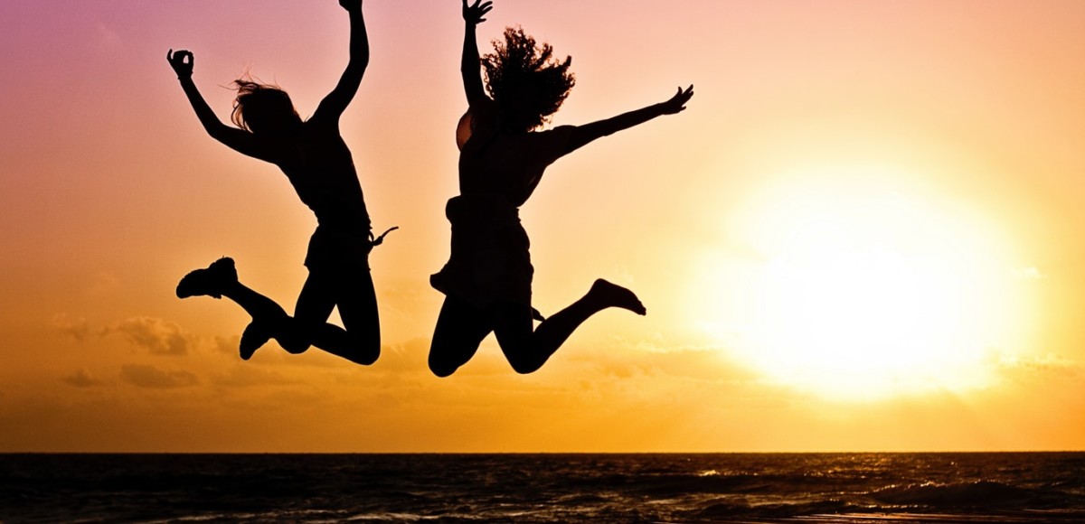 Silhouette of two people jumping with sunset and ocean in the background