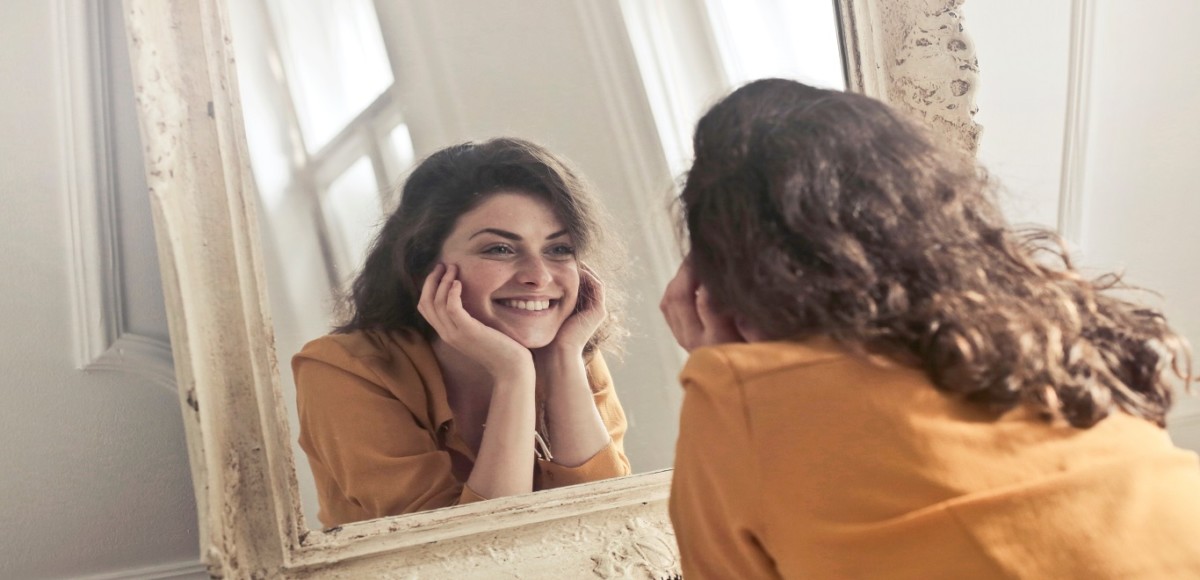 Young woman smiling into a large mirror in her studio apartment