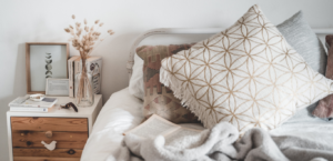 Throw pillows on a bed next to a side table with decorative items: a vase and picture frame