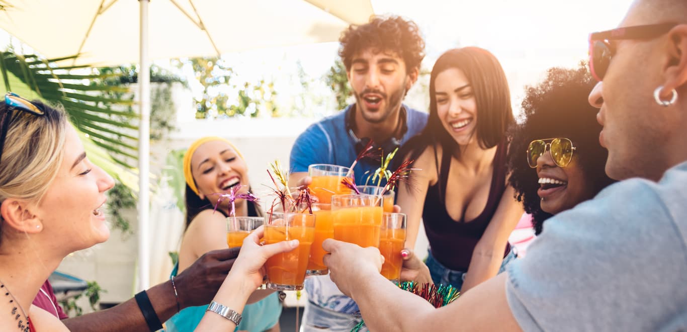 Smiling friends toasting with orange beverages around a table.