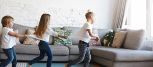 Three children chase one another in play in front of L shaped sectional couch.