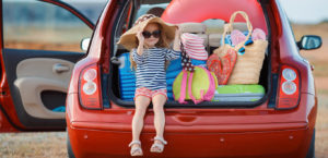 Little girl sits in back of hatchback loaded with summer gear.