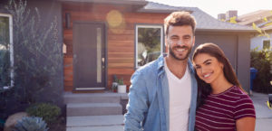 Young couple pose smiling in front of their new home.