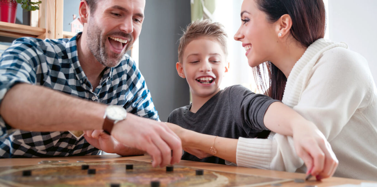 Two parents and young son smile happily while playing a board game in their bonus room.