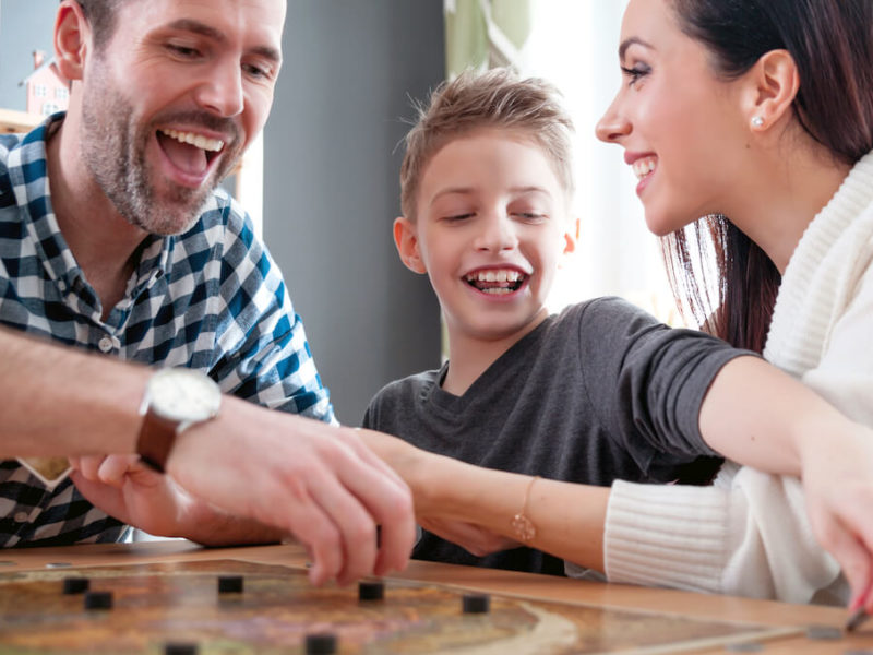 Two parents and young son smile happily while playing a board game in their bonus room.