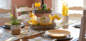 Lemon yellow accents and lemon tablescape and lemon centerpiece on wood table with white chairs.