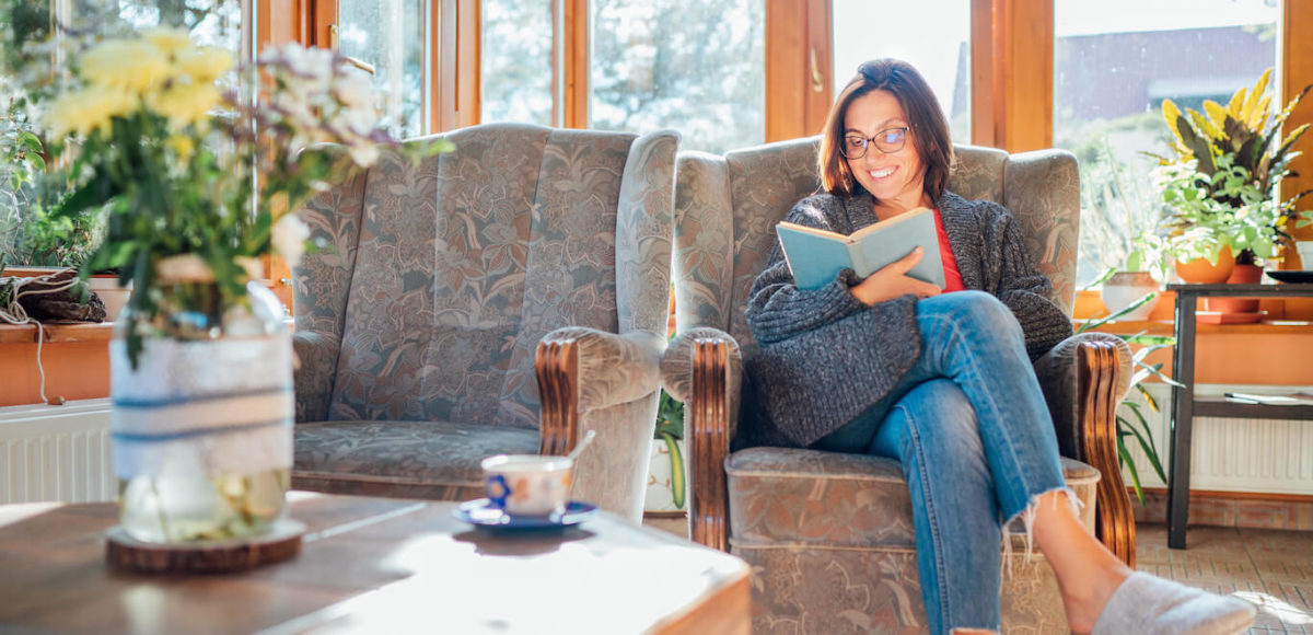 Woman relaxing reading a book on indoor sunroom furniture after learning how to decorate sunroom.