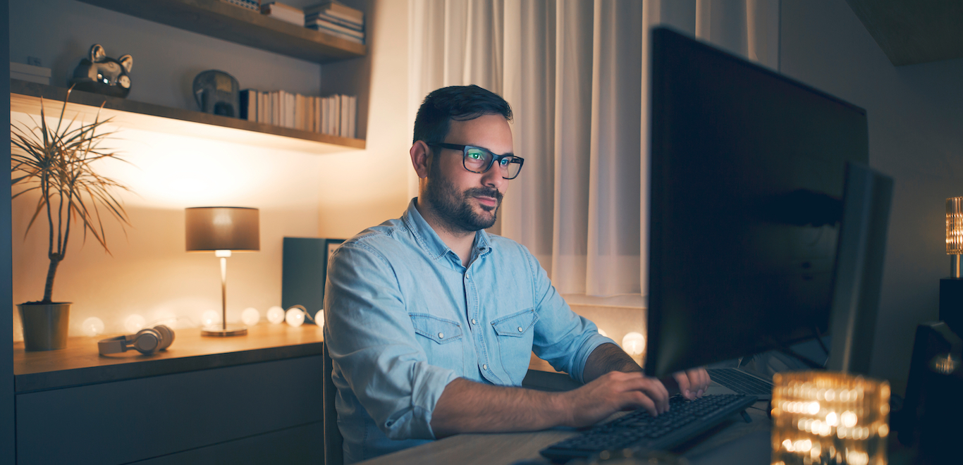 Modern young man working remotely from home at night in his basment in well decorated basement after finding basement office ideas.
