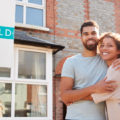 Portrait Of Excited Couple Standing Outside New Home With Sold Sign after using dos and don'ts for first time homebuyers