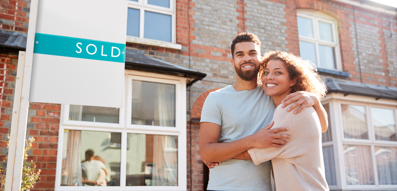 Portrait Of Excited Couple Standing Outside New Home With Sold Sign after using dos and don'ts for first time homebuyers