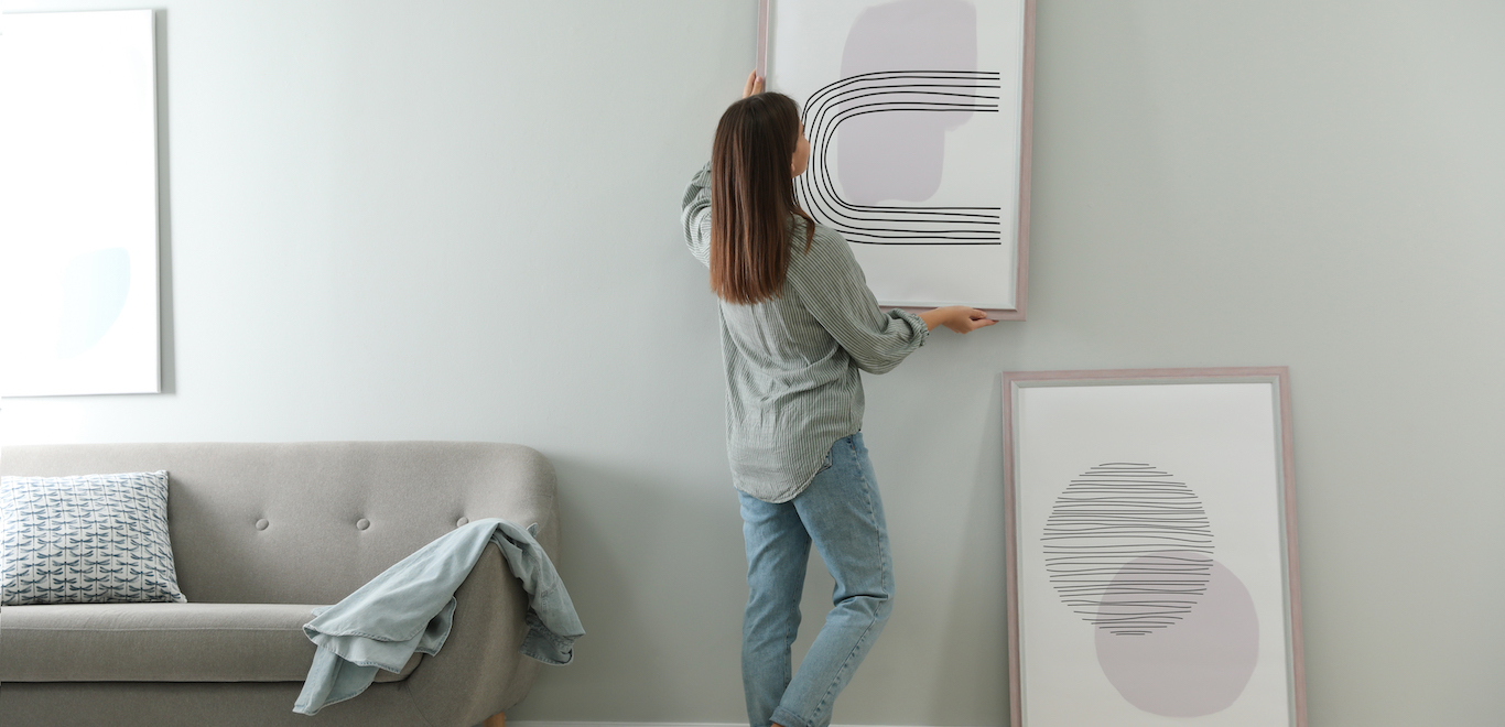 Woman hanging picture on apartment wall after figuring out how to make a rental feel like home
