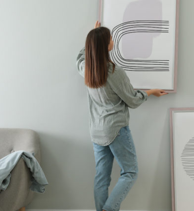 Woman hanging picture on apartment wall after figuring out how to make a rental feel like home