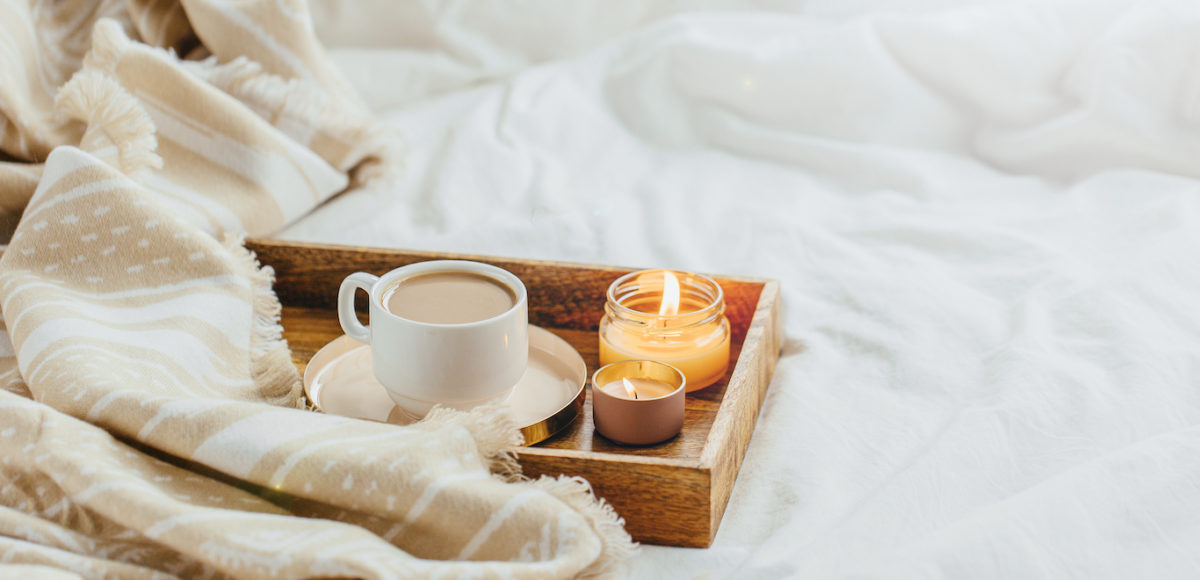 Tray of coffee and candles with warm plaid on white bedding . Breakfast in bed. Scandinavian style. Flat lay, top view