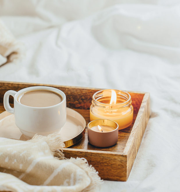 Tray of coffee and candles with warm plaid on white bedding . Breakfast in bed. Scandinavian style. Flat lay, top view