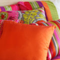 90s bedroom aesthetic created using colorful throw pillows and bedding filled with pinks, oranges, green, patterning, and different textures