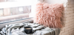 Comfy window nook with cup of coffee on a cozy gray blanket and a fluffy pink pillow