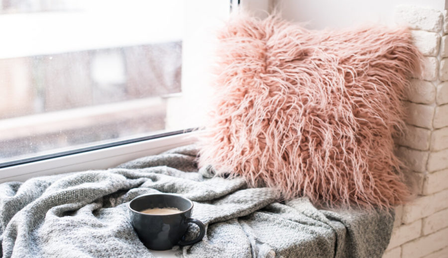Comfy window nook with cup of coffee on a cozy gray blanket and a fluffy pink pillow