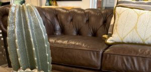 An inviting brown leather sofa with cream colored throw pillows and a large clay cactus statue in the foreground