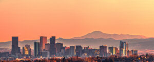 The Denver city skyline, shown at sunset, with the Rocky Mountains in the background.