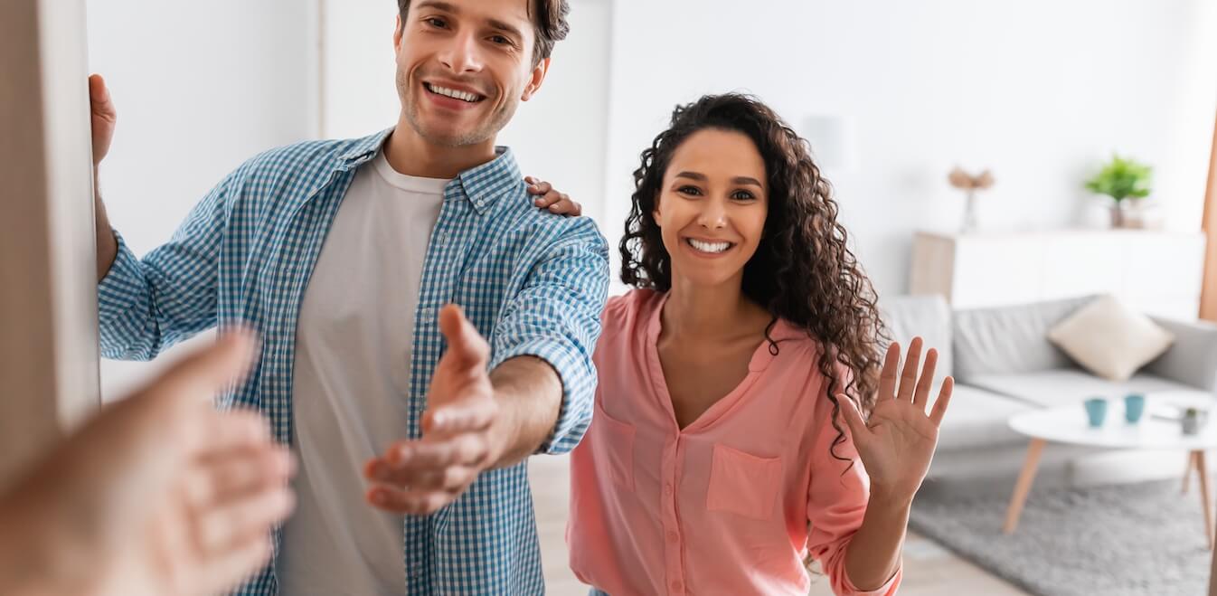 A friendly couple welcoming a neighbor into their home.