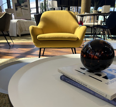 A dark purple glass orb sits on a white coffee table with a yellow chair in the background.