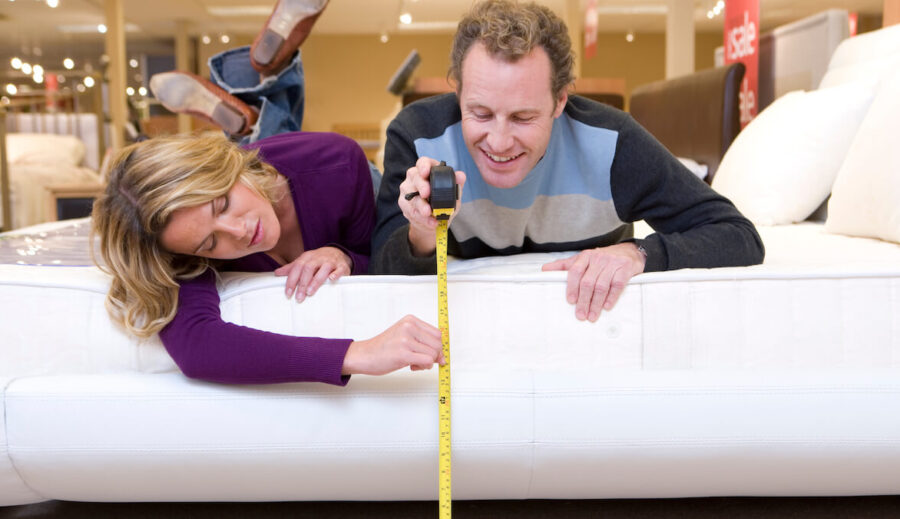 A couple measuring the size of their mattress.