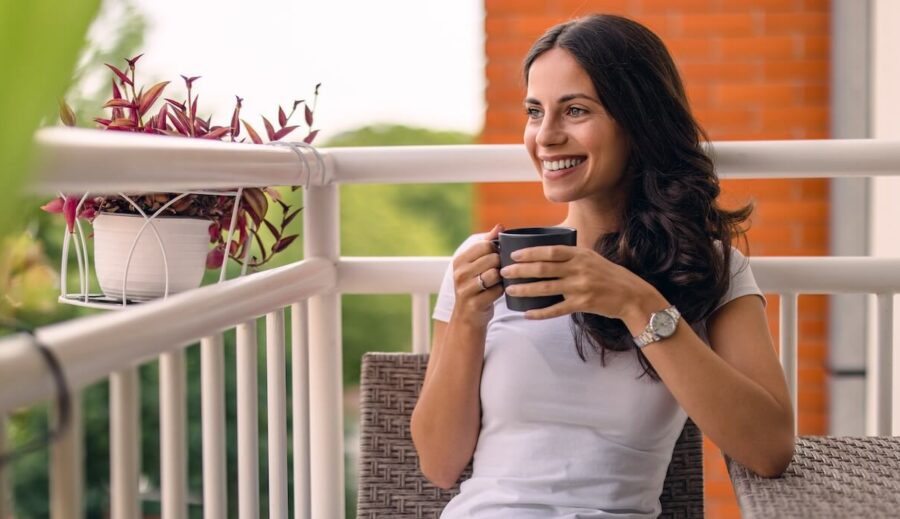 A woman enjoying a cup of coffee on her back porch, surrounded by plants and patio furniture.