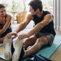 A man and woman stretch on yoga mats at home.