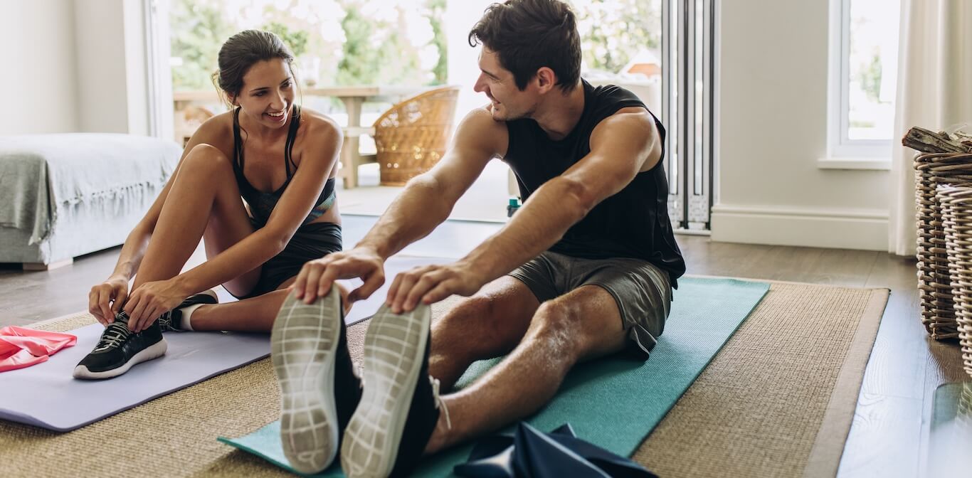 A man and woman stretch on yoga mats at home.