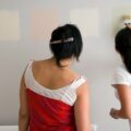 Two women looking at paint samples on a grey wall.