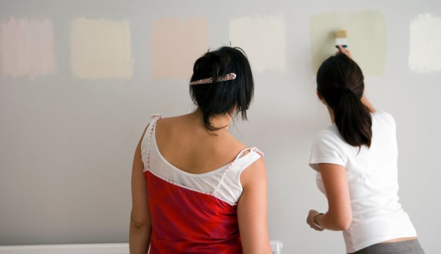 Two women looking at paint samples on a grey wall.