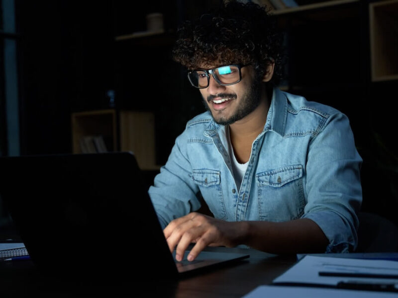 A young man takes online classes in a dark home office.