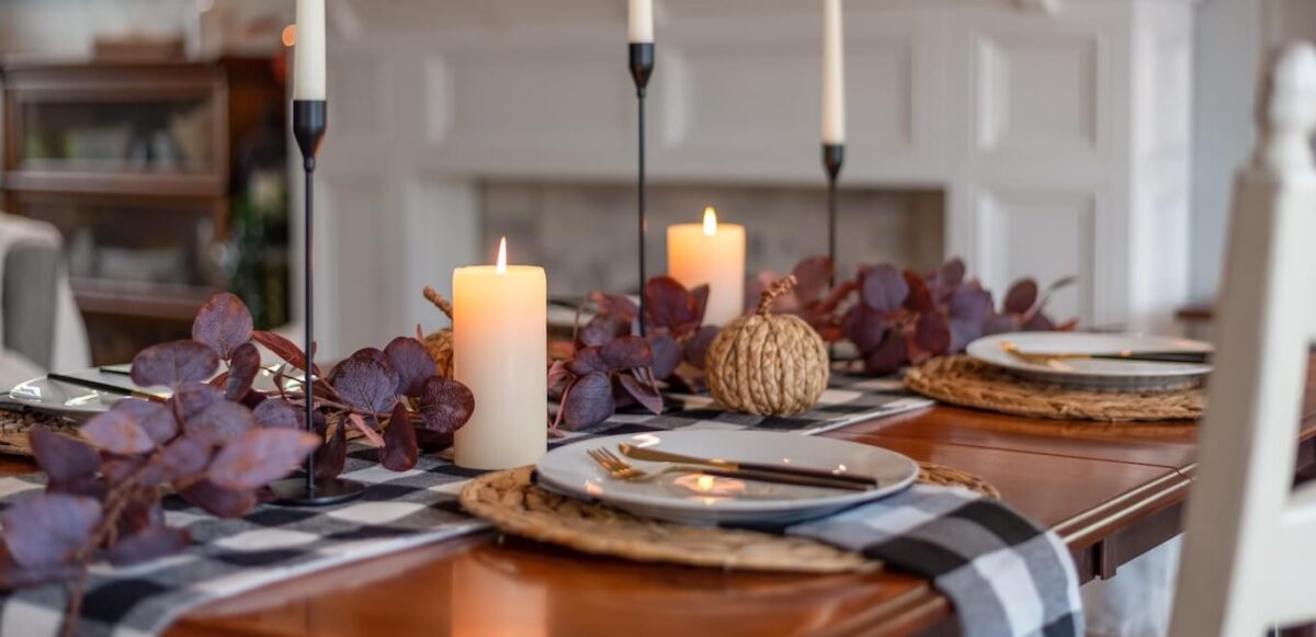 A dining room table with fall foliage and lit candles.