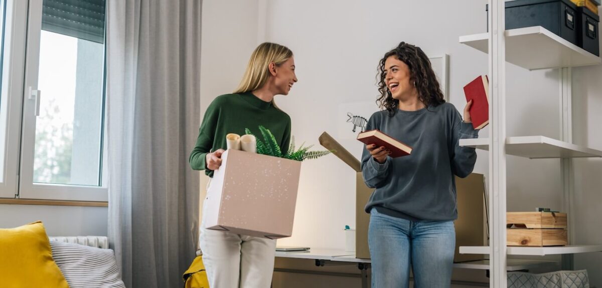 Two college roommates moving boxes into their new apartment.