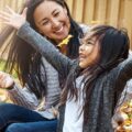 A mom and daughter play in the leaves in their yard.