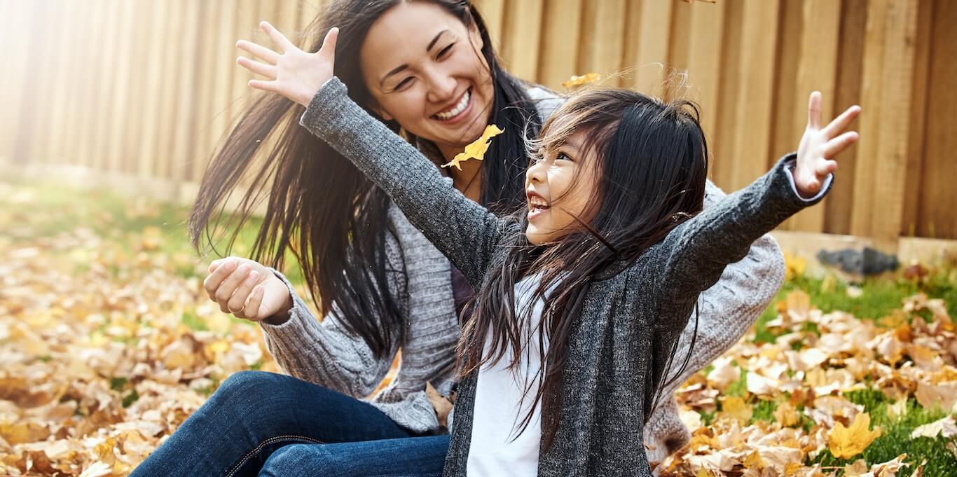 A mom and daughter play in the leaves in their yard.