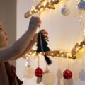 A toddler girl hanging ornaments on a tree made of lights.