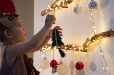 A toddler girl hanging ornaments on a tree made of lights.