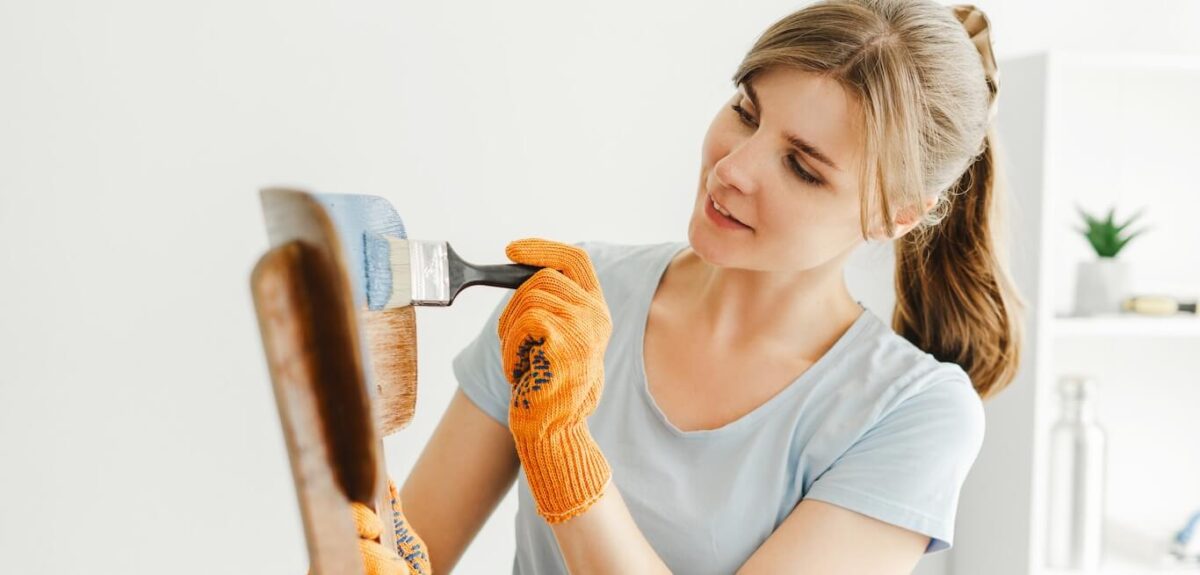 A woman stands on a ladder painting in her home.