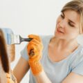 A woman stands on a ladder painting in her home.