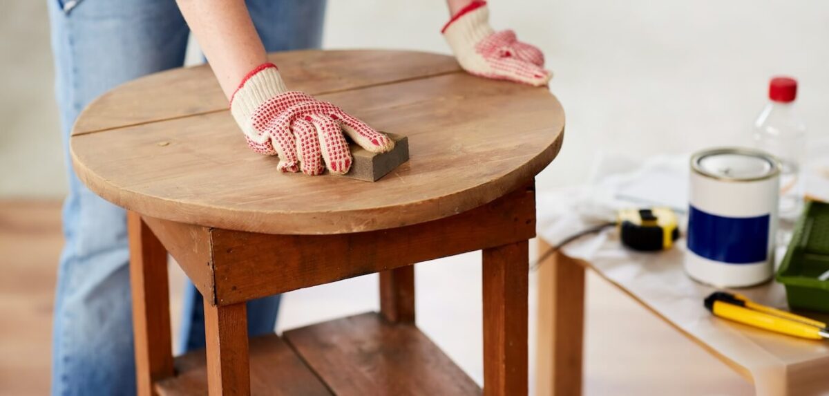 A person sanding the finish off a table before they repaint it.