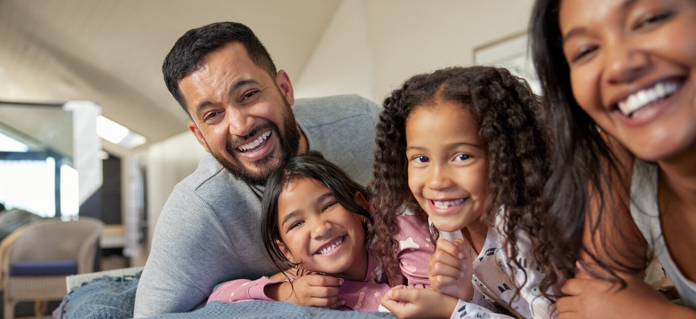 A large family sits together on a bed, laughing.