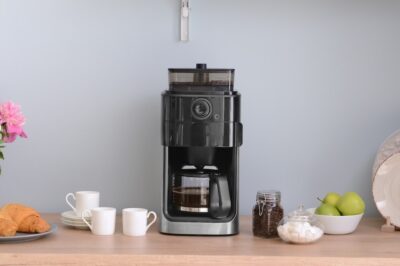 A home coffee bar with a coffee maker, coffee cups, and pastries on plates.