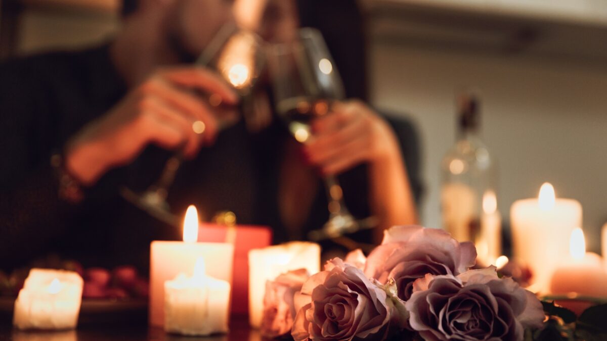 Couple toasting with wine glasses in a romantic living room with candles and roses for a cozy date night.