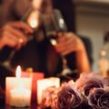 Couple toasting with wine glasses in a romantic living room with candles and roses for a cozy date night.