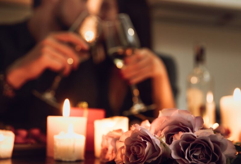 Couple toasting with wine glasses in a romantic living room with candles and roses for a cozy date night.