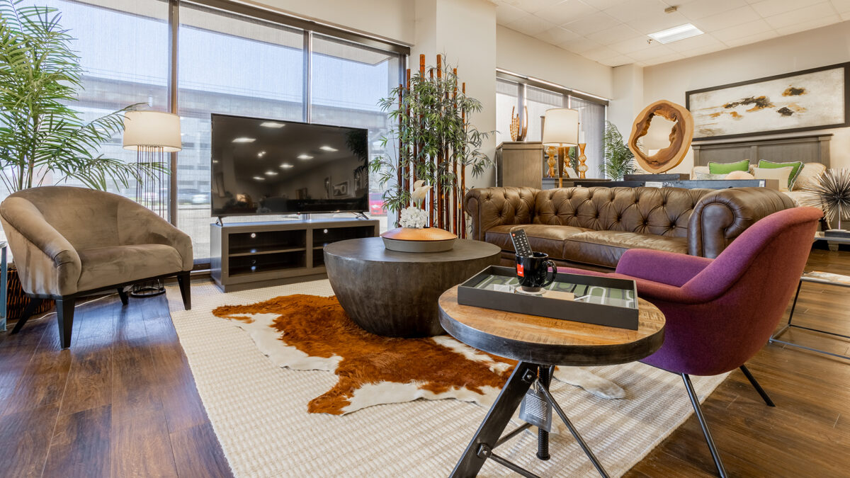 A modern living room setup with a brown leather sofa, accent chairs, a large TV stand, and decorative elements, showcasing CORT Furniture Outlet’s high-quality furniture.