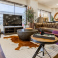 A modern living room setup with a brown leather sofa, accent chairs, a large TV stand, and decorative elements, showcasing CORT Furniture Outlet’s high-quality furniture.