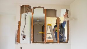 Woman after contemplating move in ready vs fixer upper house as a first time homebuyer choosing a fixer upper home doing demolition work on a wall