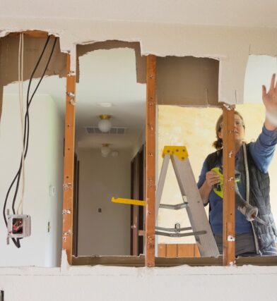 Woman after contemplating move in ready vs fixer upper house as a first time homebuyer choosing a fixer upper home doing demolition work on a wall